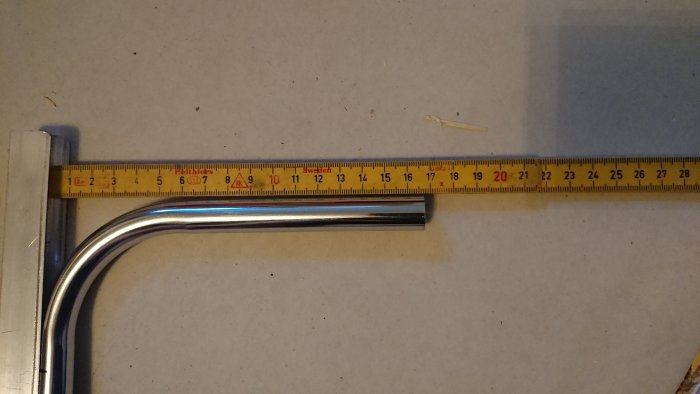 Kromat 15mm rör böjt 90 grader bredvid måttband visande längdmått och bockningsresultat.