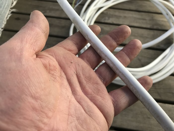 En hand håller en vit elektrisk kabel utan synlig märkning mot en bakgrund av fler kablar.