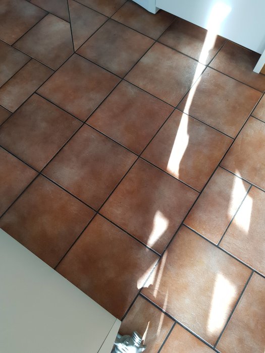 Köksgolv med 30x30 cm terrakottafärgade plattor, två spruckna och med delvis saknad fog.