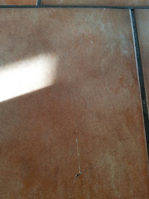 Sprucken terrakottafärgad platta med saknad fog i kök, visar tecken på åldring och slitage.