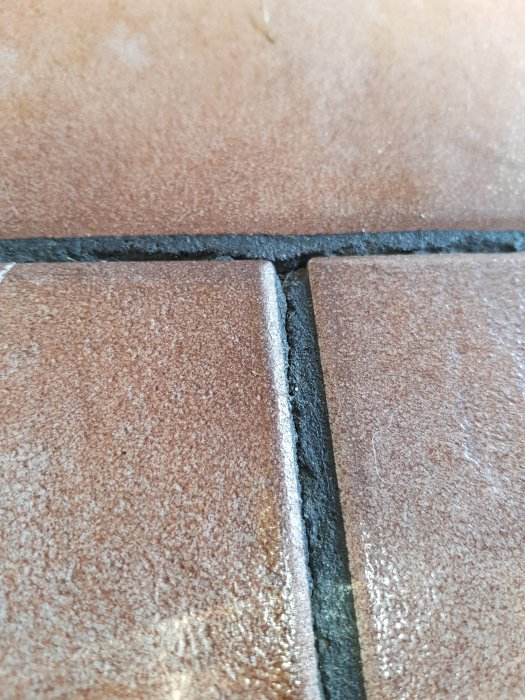 Spruckna keramikplattor på golvet med delvis försvunnen fog mellan dem.