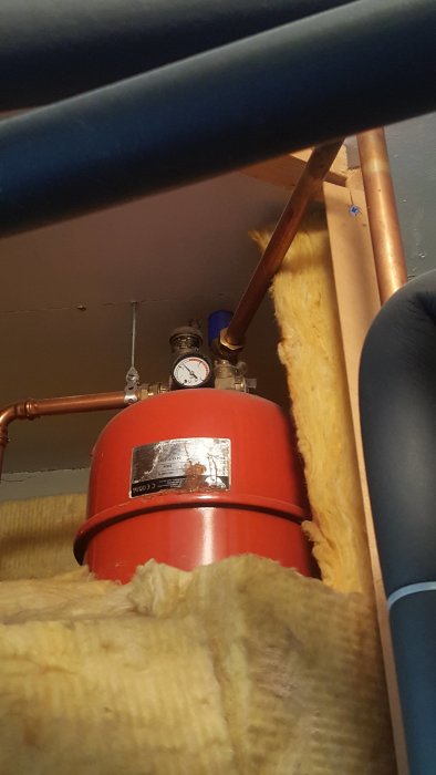 Läckande rör till höger om en varmvattenberedare omgiven av isolering i en tvättstuga.