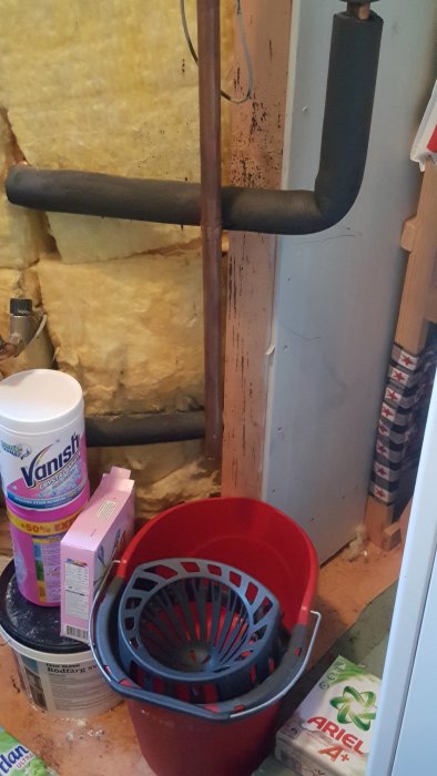 Vattenläcka från rör bredvid varmvattenberedare i tvättstuga, hink under för att samla upp droppar.