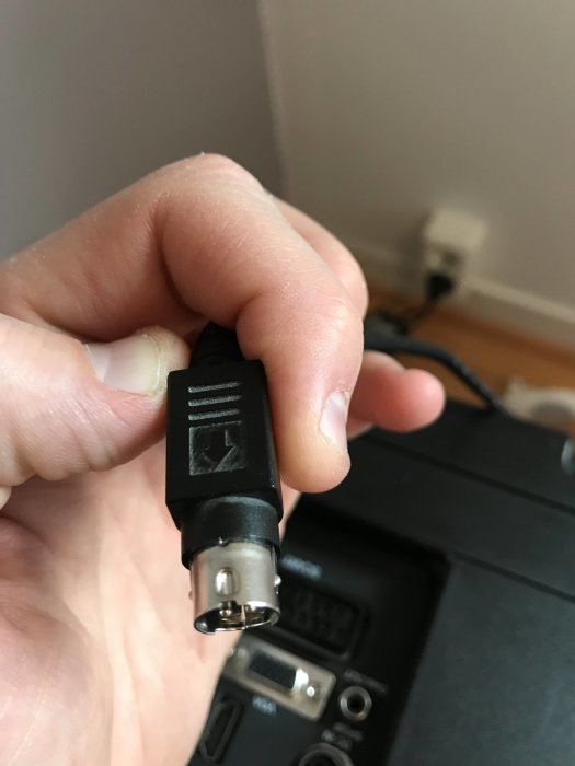 Hand håller en koaxial strömkontakt framför en TV, behov av förlängningskabel eller vinklad kontakt.