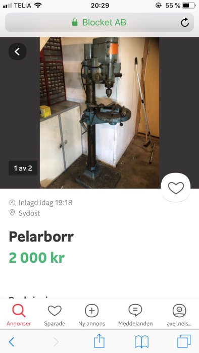 Stationär pelarborrmaskin i arbetsmiljö med vit skåp och städutrustning i bakgrunden.