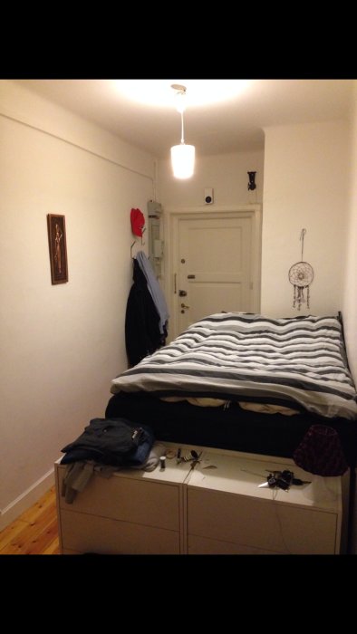 Före-bild av ett sovrum före renovering med oorganiserat skrivbord, slarvigt bäddad säng och trägolv.