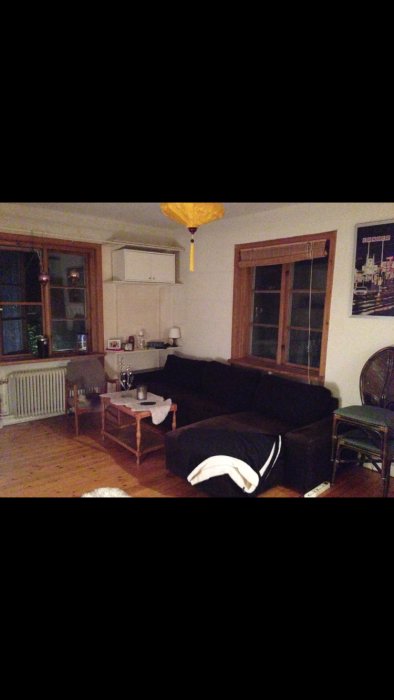 Ett orenoverat vardagsrum före renovering med mörk soffa, trägolv och gammalt fönster.