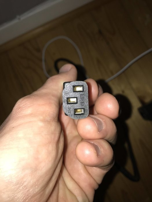 Hand håller en elektrisk kontakt med tre stift avsedd för anslutning till transformator.