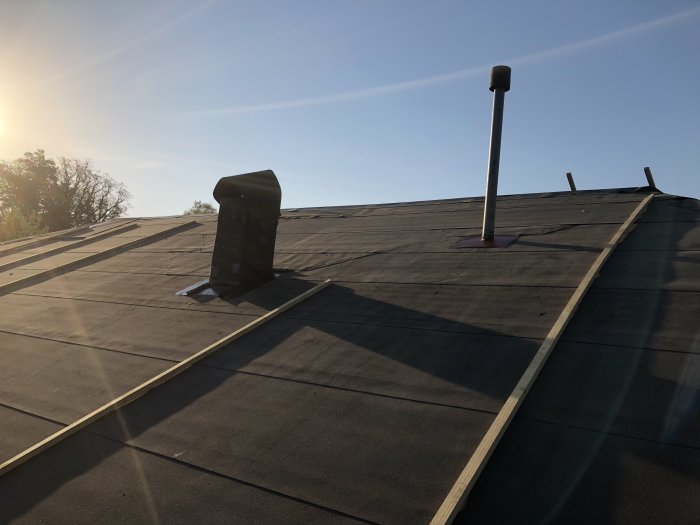 Nylagd papp på tak med skorsten och ventilationstrumma, klara för plåtarbete.