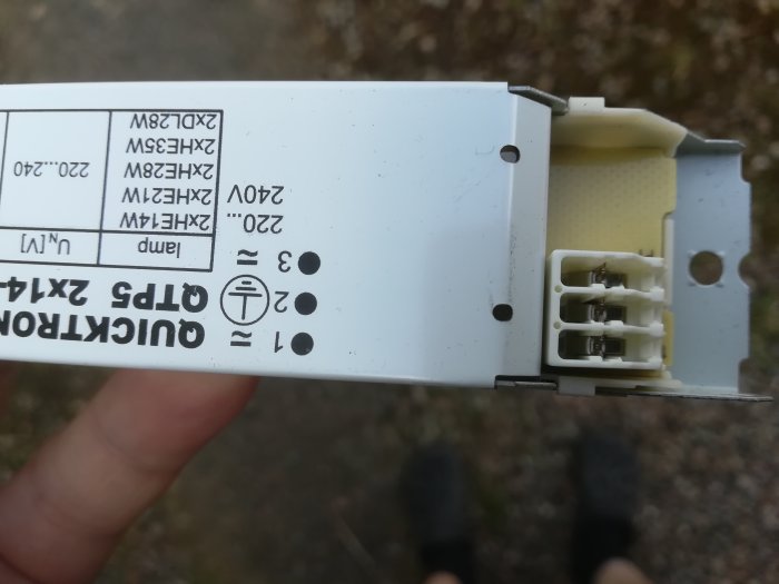Elektrisk komponent hållen i hand med teknisk etikett och synliga anslutningar, mot suddig bakgrund.
