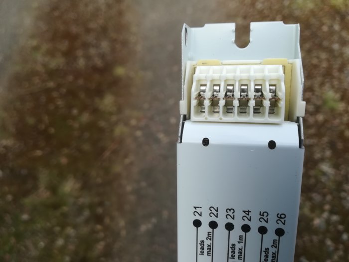 Närbild av en vit elektrisk anslutningsmodul med märkningar och anslutningspunkter.