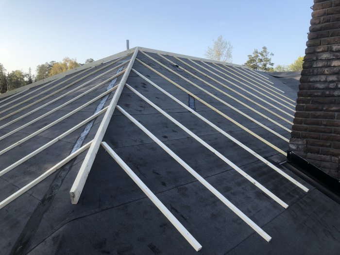 Montering av takläkt och nockbräda på ett lutande hustak i byggproces.