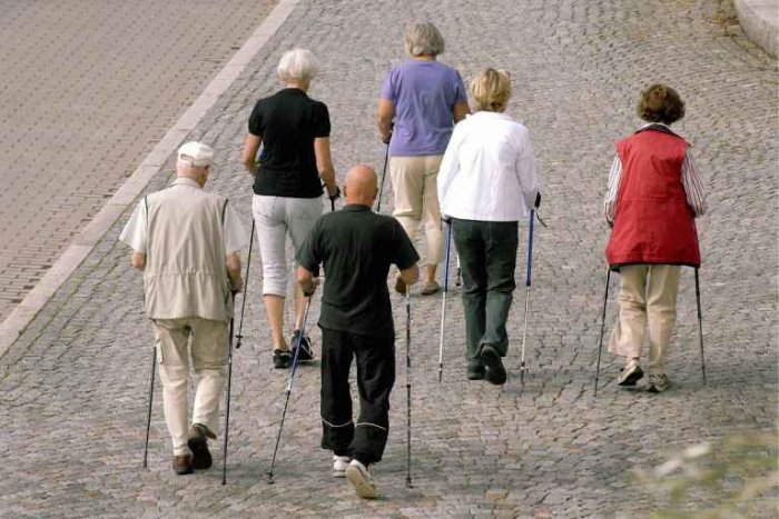 Grupp av äldre personer som deltar i nordisk gång på en kullerstensbelagd väg.