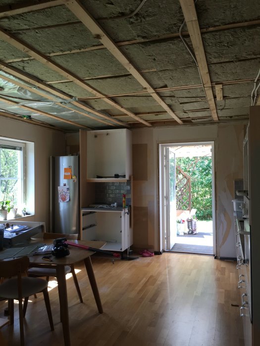 Renoverat kök med avlägsnat innertak som visar träbjälkar och isoleringsmaterial, delvis plastad yta vid yttervägg.