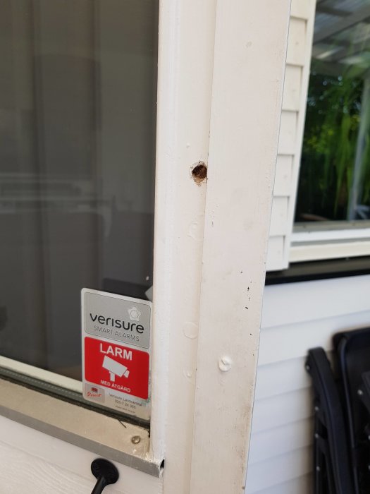 Vitmålad dörrkarm med övermålade skruvar och ett synligt metallobjekt, samt ett larmdekaler.