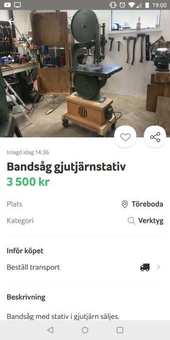 Grön bandsåg med gjutjärnsstativ i en verkstad med verktyg och bänkar i bakgrunden.