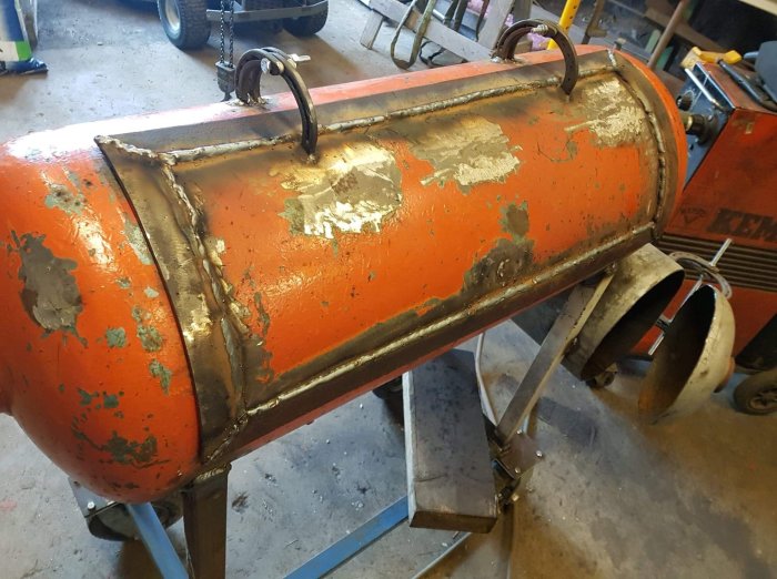 Svetsade metallister på en sliten, orange behållare med en lyftarm monterad överst.