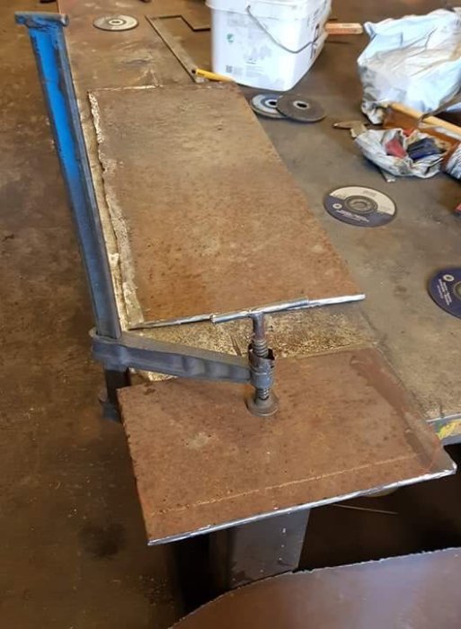 Avkapad plåtbit med böjning fixerad mot en större plåt i en verkstadsmiljö.