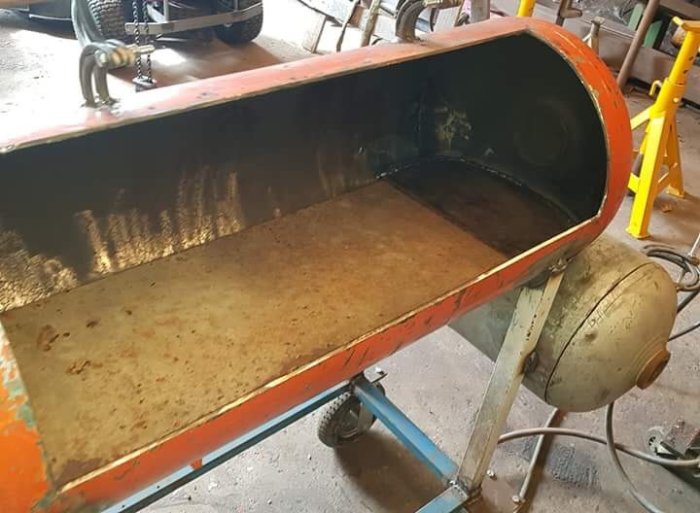 En böjd stor metallplåt i en verkstadsliknande miljö med hydraulisk press efter modifikation.
