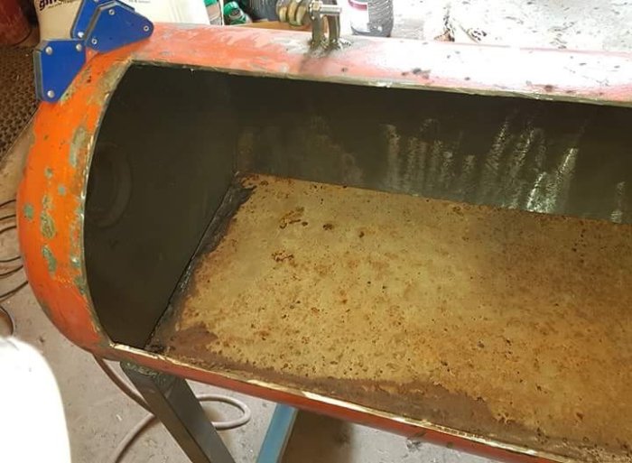En stor plåt böjd i mitten inne i en orangeröd metallkonstruktion, avsedd för att leda fett centralt.