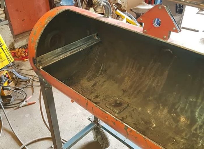 Hyllplan nr 1 monterat inuti en orange metallbehållare på verkstadsbord med svetsutrustning i bakgrunden.