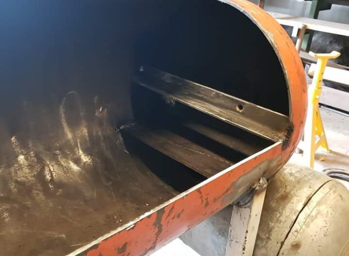 Grova u-järn använda som hyllplan i en stor, rund, öppen behållare med sliten orange färg.