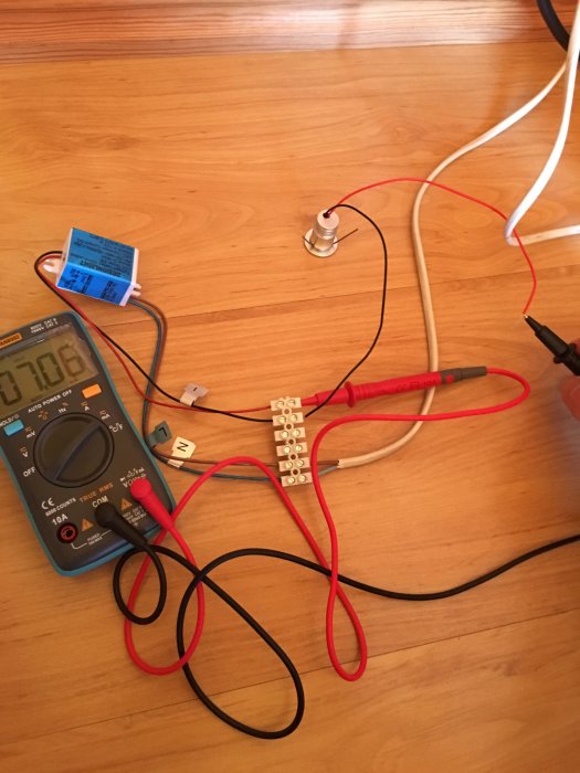 Multimeter ansluten till en strömkabel och en lampa på ett trägolv.