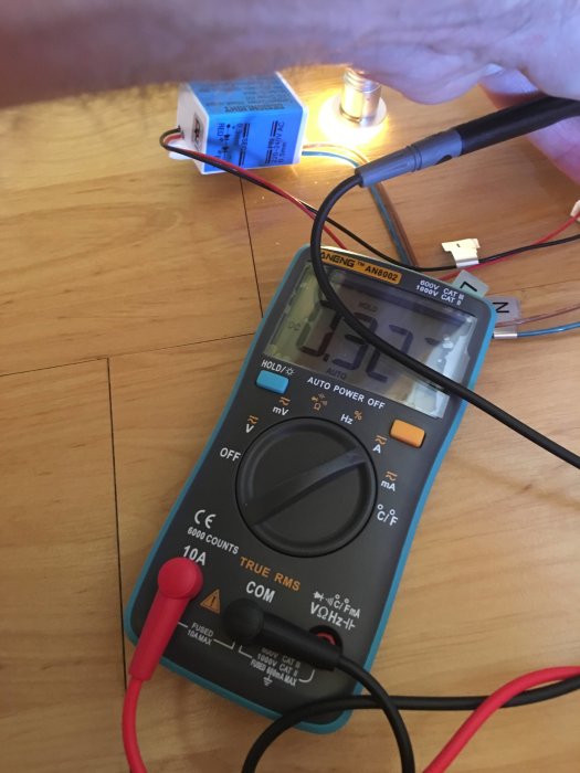 Multimeter ansluten till elektronisk komponent med tänd LED-lampa i bakgrunden.
