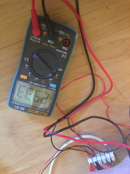 Multimeter som visar spänning med flera kablar och anslutningar på trägolv.