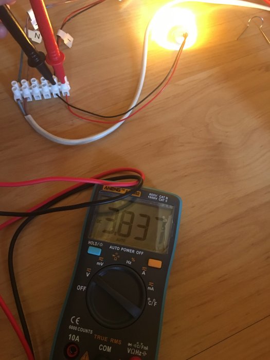 Multimeter som visar 3.84V med en glödlampa ansluten till en kabel, vilket indikerar hög spänning.