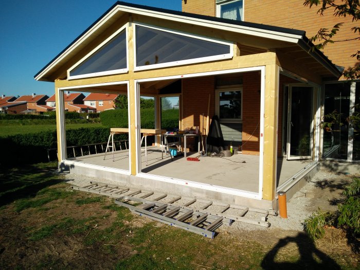 Byggarbetsplats med nyinstallerade karmar till skjutpartier för veranda under konstruktion, med verktyg och material synligt.