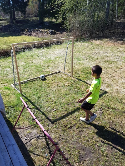 Barn spelar fotboll med hemmagjort mål av trä och nät i trädgården.