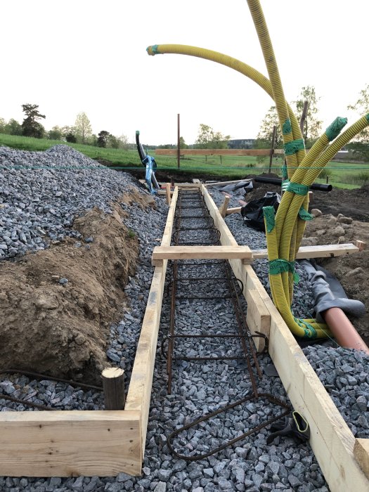 Armeringsjärn och byglar i grunden för ett byggprojekt, omliggande grus och byggmaterial.