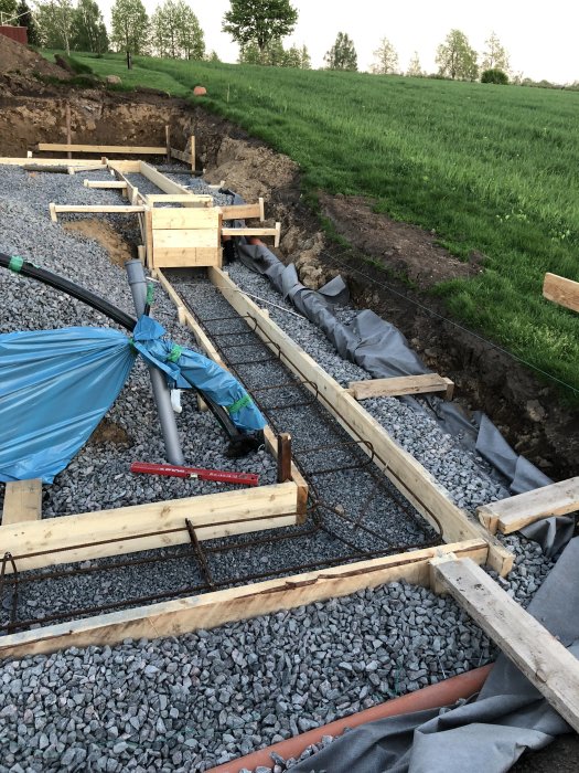 Armeringsjärn i grunden för ett byggprojekt med grus och träformar på en byggarbetsplats.
