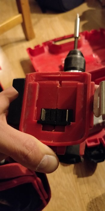 Närbild av en skruvdragares batterianslutning med två av fem synliga kontakter i fokus, mot en röd verktygsväska.