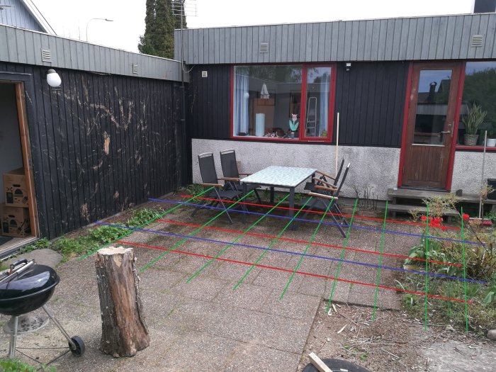 Trädgård med målade röda, gröna och blå streck för att planera placering av reglar och trall på en terrass.
