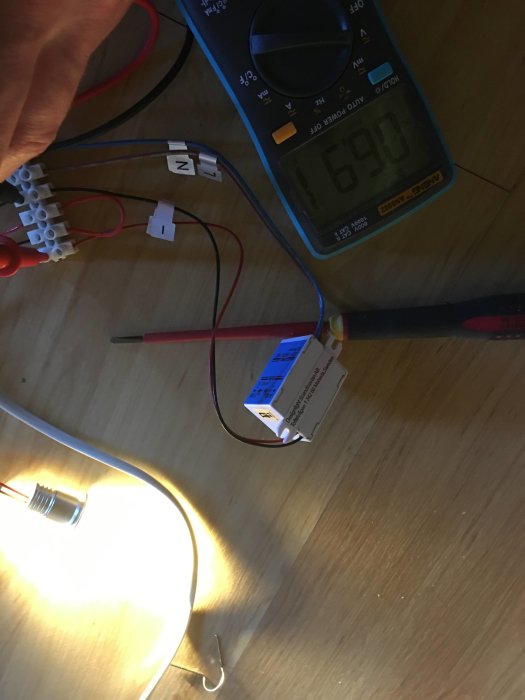 Multimeter som visar 1,69 volt, kopplad till en LED-driver och en lysande LED-lampa i ett elektronikprojekt.