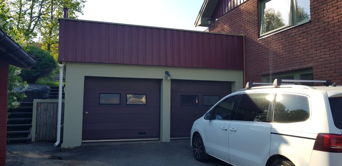 Ett rödbrunt garage i betong med terrass ovanpå, vid ett suteränghus, tänkt för spabadsinstallation.