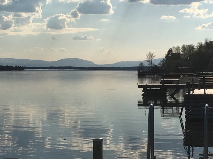 Kvällsvy vid bryggan med spegelblank sjö och Bydalsfjällen i horisonten.