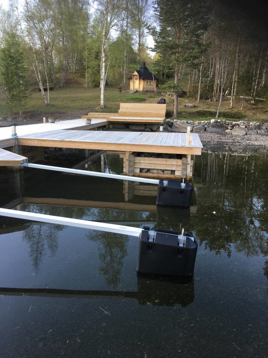 Översvämmad trädgård med en brygga som delvis står under vatten, reflekterande träd i bakgrunden.