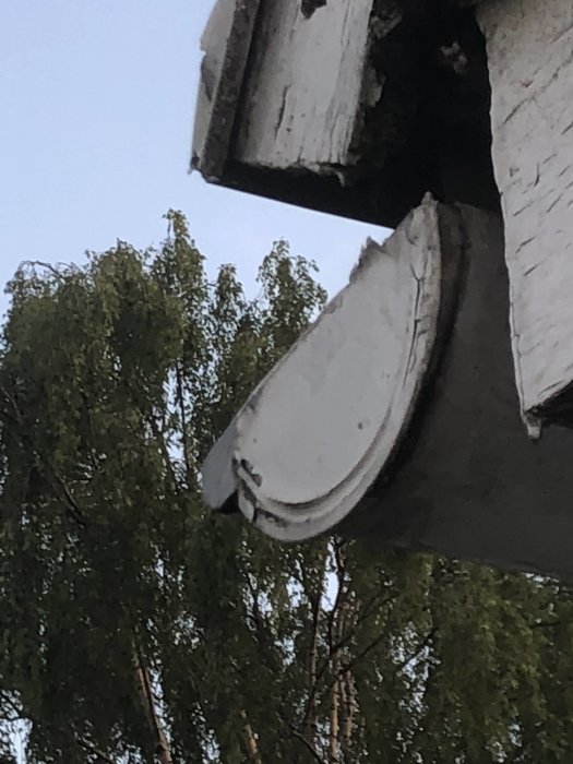 Närbild på en grå ränngavel under takavsats med träd i bakgrunden.