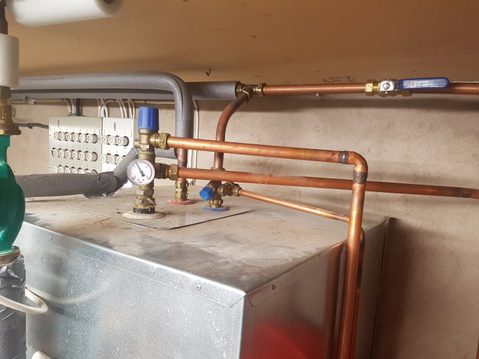 Installation av blandningsventil med grå och vit rörisolering, kall- och varmvattenrör, och en värmefördelare.