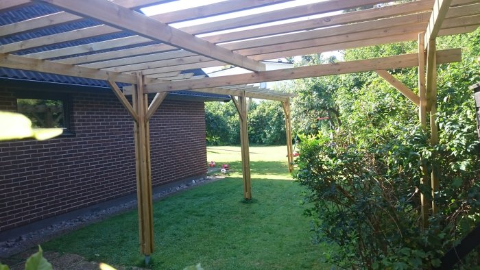 Hembyggd pergola med knippepelare och 45mm distans, placerad i en trädgård vid ett tegelhus.