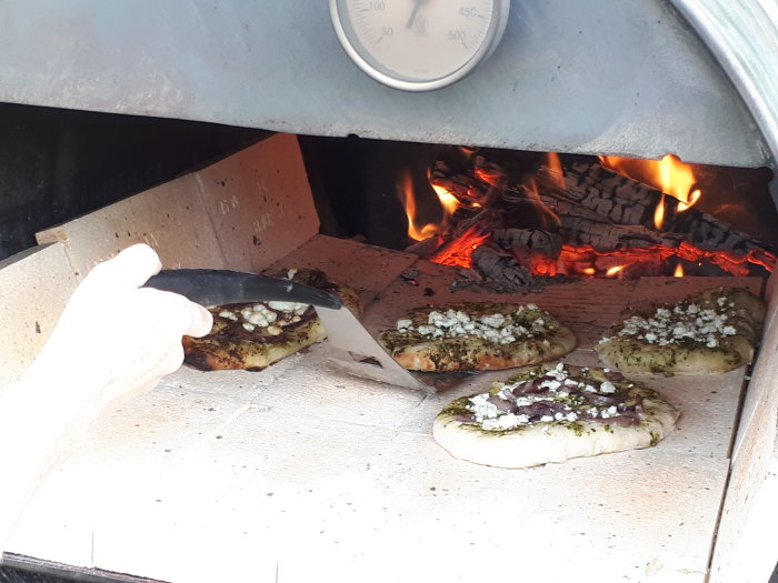 Flatbröd bakas i hemmagjord vedeldad ugn, med en hand som använder en spatel och en termometer som visar 450 grader.