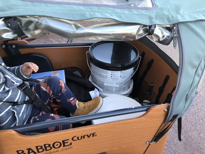 Barn i en trehjulig lastcykel med färgburkar, Babboe Curve-logga synlig.
