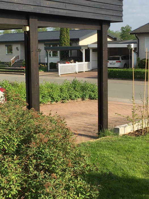 Del av carport med visning av stolpe och tak mot en bakgrund av bostad och grönska.