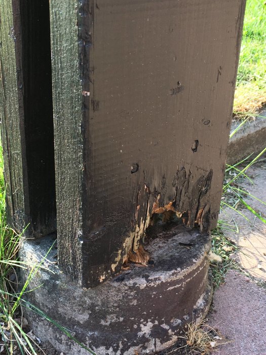 Murkna träreglar vid basen av en carportstolpe, där trä möter betongplint och visar tecken på förfall.