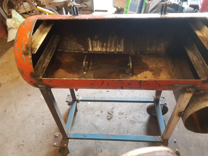 Svetsad plattjärnsram och handtag på en deformerad metallplåt i en orange byggmaskin.
