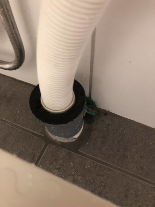 Vit avloppsröranslutning till golv med tätningsproblem.