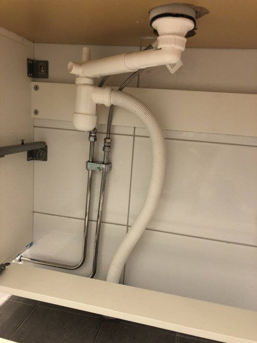 Undersida av handfat med synliga rör och avloppssystem i vit och silverkategori.